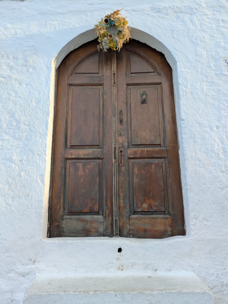 Eine schöne braune Holztür mit einem Blumenkranz in einer weißen Kalkwand